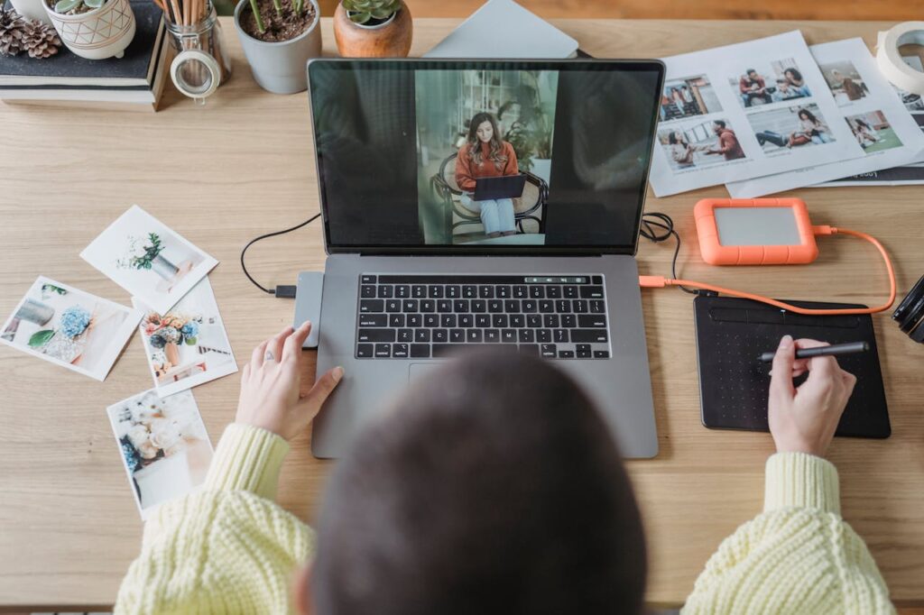 Overhead view of a creative workspace featuring a laptop, tablet, and photo editing accessories.